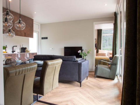Intérieur de lodge moderne avec cuisine ouverte, table à manger, salon cosy et vue sur la chambre.