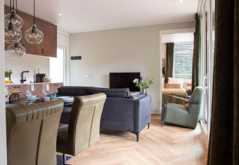 Intérieur de lodge moderne avec cuisine ouverte, table à manger, salon cosy et vue sur la chambre.