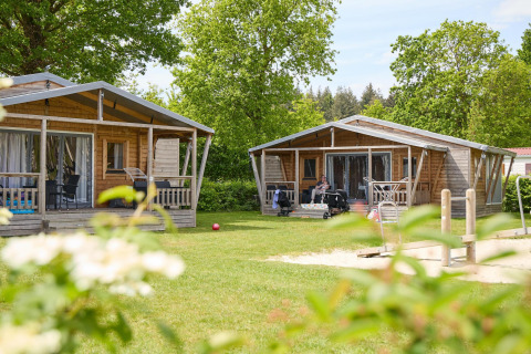 Deux tentes safari en bois au Camping 't Veld aux Pays-Bas, entourées de verdure et d'une aire de jeux.