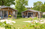 Deux tentes safari en bois au Camping 't Veld aux Pays-Bas, entourées de verdure et d'une aire de jeux.
