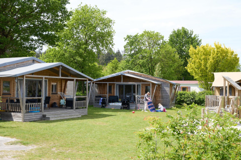Tentes safari et cabanes en bois au Camping 't Veld aux Pays-Bas, entourées de pelouse et d’arbres verts.