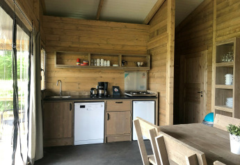 Modern safari tent kitchen interior with wooden furniture, stove, dishwasher, and dining area at Camping 't Veld.