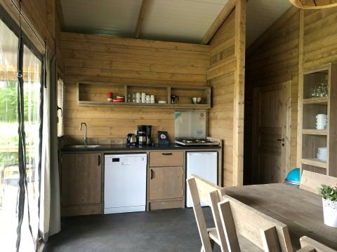 Moderne safaritentkeuken met houten meubels, fornuis, vaatwasser en eethoek op Camping 't Veld.