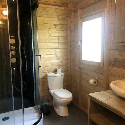Baño moderno de madera con ducha, inodoro, ventana y lavabo en safari tent de Camping 't Veld, Países Bajos.