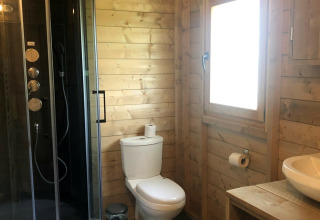 Baño moderno de madera con ducha, inodoro, ventana y lavabo en safari tent de Camping 't Veld, Países Bajos.