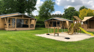 Tentes safari et aire de jeux sablée au Camping 't Veld aux Pays-Bas sous un ciel ensoleillé.