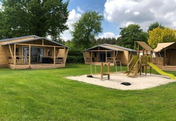 Trætelthuse og legeplads med sandkasse på Camping 't Veld i Holland under en klar himmel.