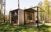 Acogedora cabaña de madera llamada Classic con ventanales grandes y terraza en un bosque frondoso.