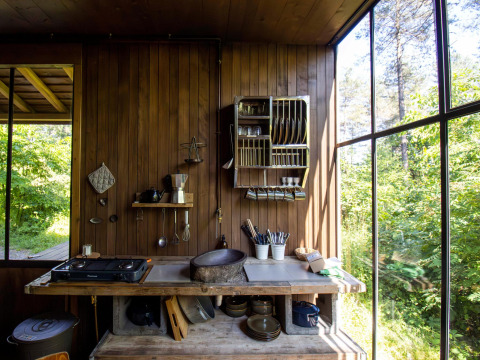 Cocina rústica de cabaña con paredes de madera, grandes ventanas y vista a la exuberante naturaleza exterior.