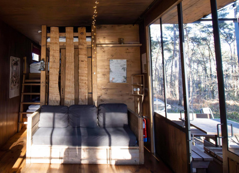 Helles Wohnzimmer in einer klassischen Hütte mit Holzdetails, Sofa und großen Fenstern zum Wald.