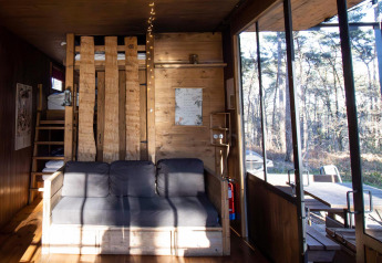 Salon lumineux de la cabine Classic avec canapé, murs en bois et grandes baies vitrées donnant sur la forêt.