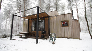 Moderne houten hut in een besneeuwd bos met terras, barbecue en sfeerverlichting in de winter.