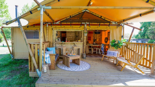 Gemütliche Veranda des Safarizelts Dune Lodge im Sandberghe in den Niederlanden, mit Holzterrasse und Sitzbereich.