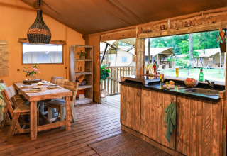 Cozy kitchen and dining area inside a safari tent at Dune Lodge, Sandberghe, Netherlands, with outdoor view.