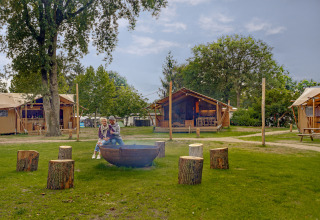 Older couple sitting by fire pit at Dune Lodge safari tent in Sandberghe, the Netherlands, on grass.
