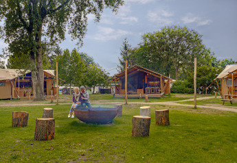 Older couple sitting by fire pit at Dune Lodge safari tent in Sandberghe, the Netherlands, on grass.
