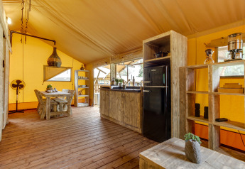 Indretning i safariteltet Dune Lodge på Sandberghe i Holland med trægulv, køkken og spiseplads.