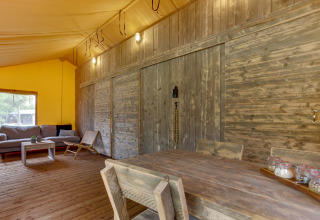 Interieur van safaritent Dune Lodge bij Sandberghe, Nederland, met rustieke houten meubels en gezellige zithoek.