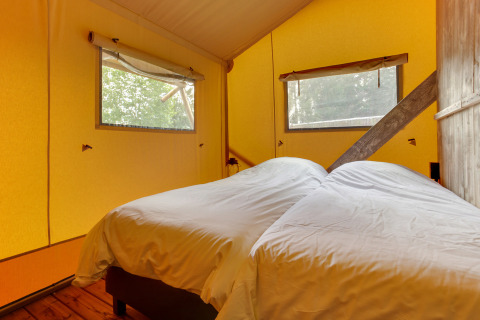 Interior of a safari tent bedroom with two single beds, yellow walls, and large windows.