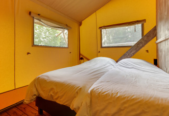 Interior of a safari tent bedroom with two single beds, yellow walls, and large windows.