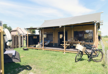Alojamiento de glamping moderno con porche cubierto, bicicleta y zona de descanso sobre césped soleado.