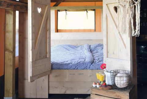 Alloggio glamping accogliente con letto in legno, biancheria a quadretti e colazione rustica.