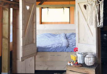 Cozy glamping accommodation with a wooden framed bed, checkered bedding, and a rustic breakfast setup.