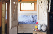 Cozy glamping accommodation with a wooden framed bed, checkered bedding, and a rustic breakfast setup.