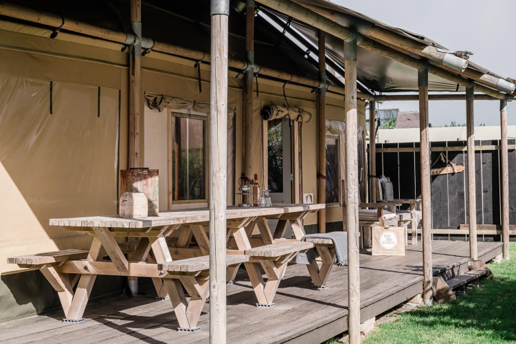 Terraza de madera con mesas de picnic en Beach Lodge Big, Duynpark Het Zwanenwater, Países Bajos.