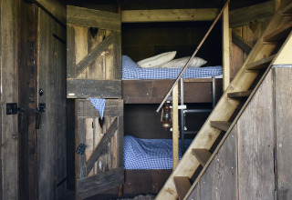 Accogliente stanza glamping con letti a castello in legno, biancheria a quadretti e scala rustica.