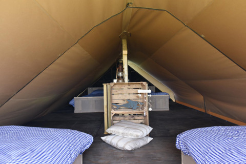 Intérieur d'une tente lodge confortable avec literie à carreaux bleus et coussins sur un plancher en bois.