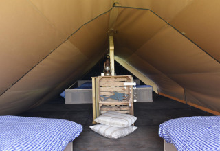 Interior de una tienda tipo lodge con ropa de cama azul a cuadros y cojines sobre el suelo de madera.