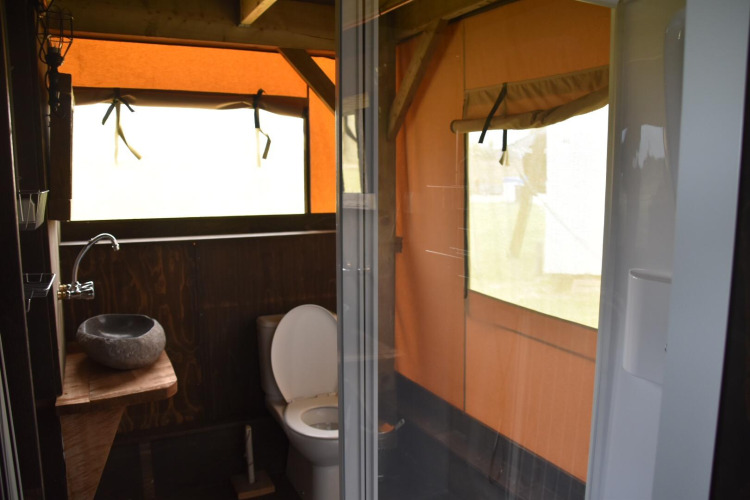 Baño en una cabaña con inodoro, lavabo de piedra y ducha, rodeado de paredes tipo tienda de campaña.