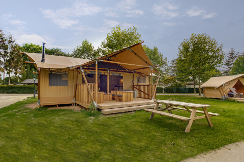 Safari-Zelt Dune Lodge bei Sandberghe in den Niederlanden, mit Holzterrasse und Picknicktisch auf Rasen.