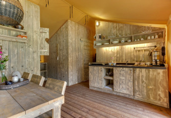 Rustic wooden kitchen inside a safari tent at Dune Lodge, Sandberghe, Netherlands, with dining table.