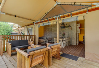 Überdachte Holzterrasse mit Sitzbereich und Esstisch im Safari-Zelt Dune Lodge in Sandberghe, Niederlande.
