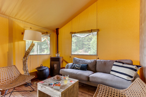 Interior de la tienda safari Dune Lodge en Sandberghe, Países Bajos, con sofá, sillas y decoración rústica.