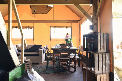 Vista interior de una tienda glamping con muebles de madera, sofá, mesa de comedor y luz natural.