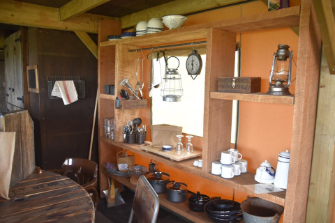 Cocina rústica con estantes de madera, vajilla, ollas y farol en Beach Lodge Luxury, Duynpark Het Zwanenwater, Países Bajos.