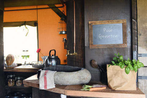Angolo cucina rustico in lodge con lavabo in pietra, erbe aromatiche e lavagna con 'Puur Genieten'.