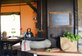 Cocina rústica de cabaña con fregadero de piedra, hierbas frescas y cartel que dice 'Puur Genieten'.