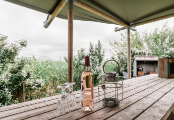 Tavolo in legno con bottiglia di vino, due bicchieri e lanterna alla Beach Lodge Luxury, Duynpark Het Zwanenwater, Paesi Bassi.