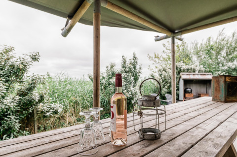 Wooden table with a wine bottle, two glasses, and lantern at Beach Lodge Luxury, Duynpark Het Zwanenwater, Netherlands.