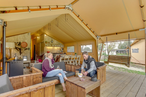 Due persone si rilassano nella tenda safari Forest Lodge a Sandberghe, Paesi Bassi, su arredi in legno.
