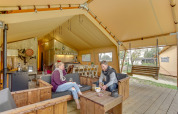 Dos personas se relajan en una tienda safari Forest Lodge en Sandberghe, Países Bajos, con muebles de madera.