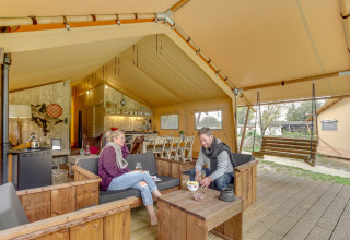 Dos personas se relajan en una tienda safari Forest Lodge en Sandberghe, Países Bajos, con muebles de madera.