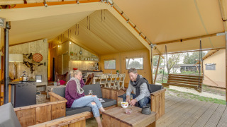 Dos personas se relajan en una tienda safari Forest Lodge en Sandberghe, Países Bajos, con muebles de madera.