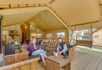 Twee mensen genieten van de Forest Lodge safaritent bij Sandberghe in Nederland, met houten zitmeubilair.