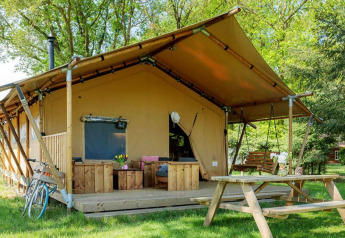Safari telt Forest Lodge ved Sandberghe i Holland, med terrasse, bænk og picnicbord i grønne omgivelser.