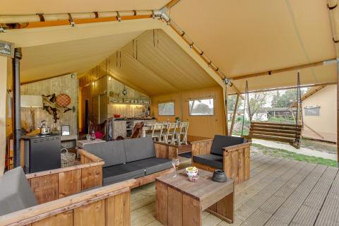 Interior de la tienda safari Forest Lodge en Sandberghe, Países Bajos, con sala y banco colgante de madera.